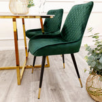 Green velvet dining chair with diamond-tufted back, curved arms, and tapered black legs.