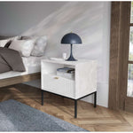 White bedside table in a living room, with ribbed drawer front and open shelf.