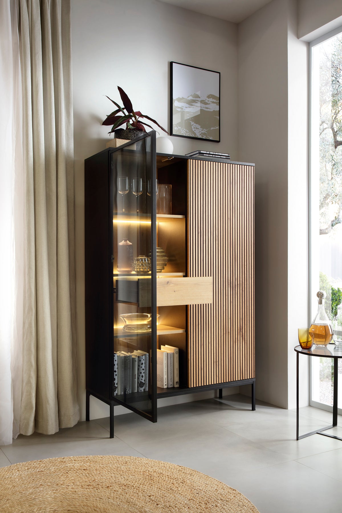 High display cabinet in black frame with wood slatted door and glass shelves lit inside