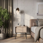 Small bedside cabinet with ribbed drawer front, light wood finish with black legs in room