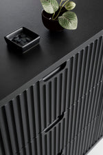 Mila TV cabinet close-up: dark fluted front with curved handles and tabletop accessories.