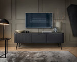 Mila TV cabinet in dark finish with fluted doors, slim legs, and media setup styling.