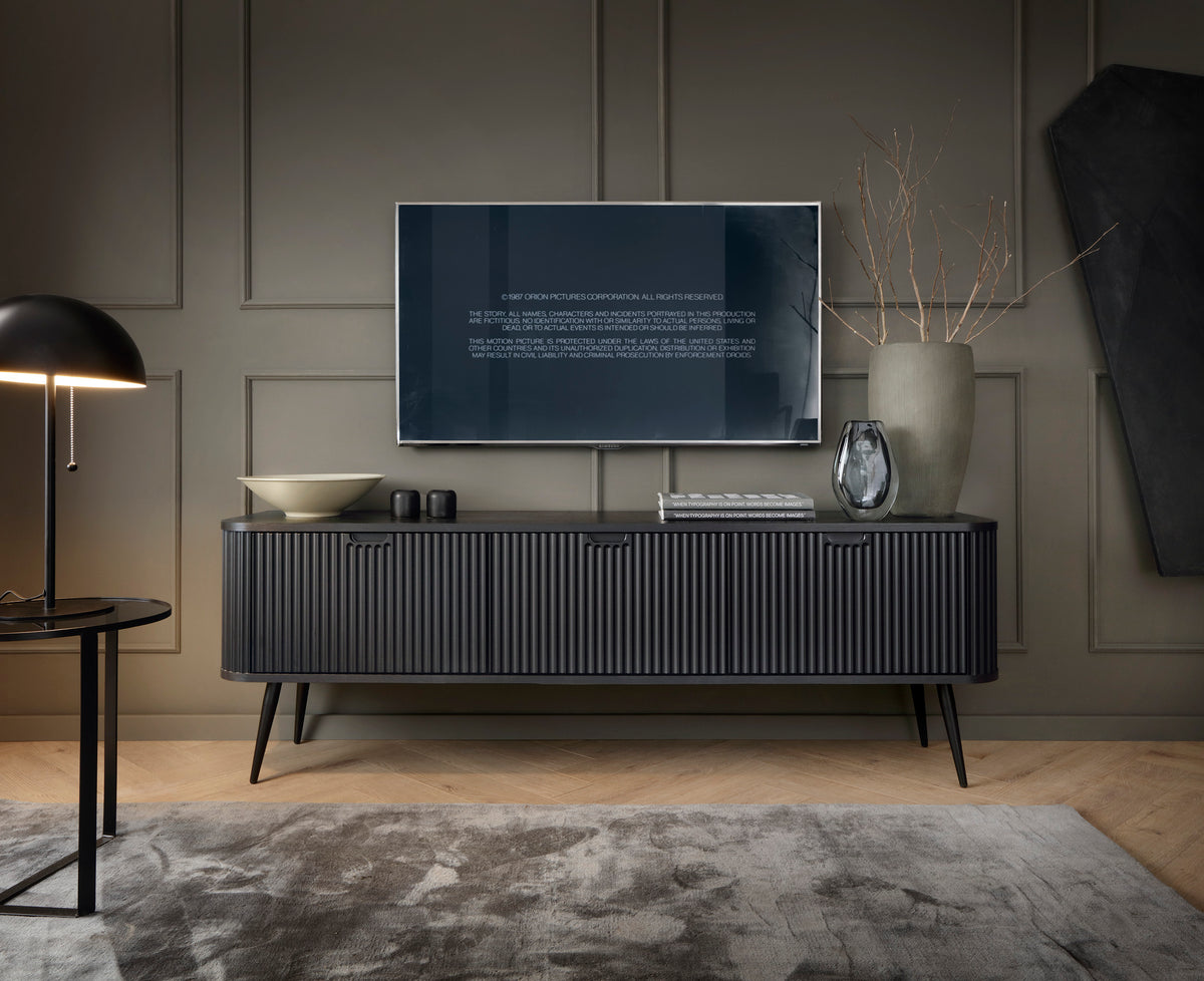 Mila TV cabinet in dark finish with fluted doors, slim legs, and media setup styling.