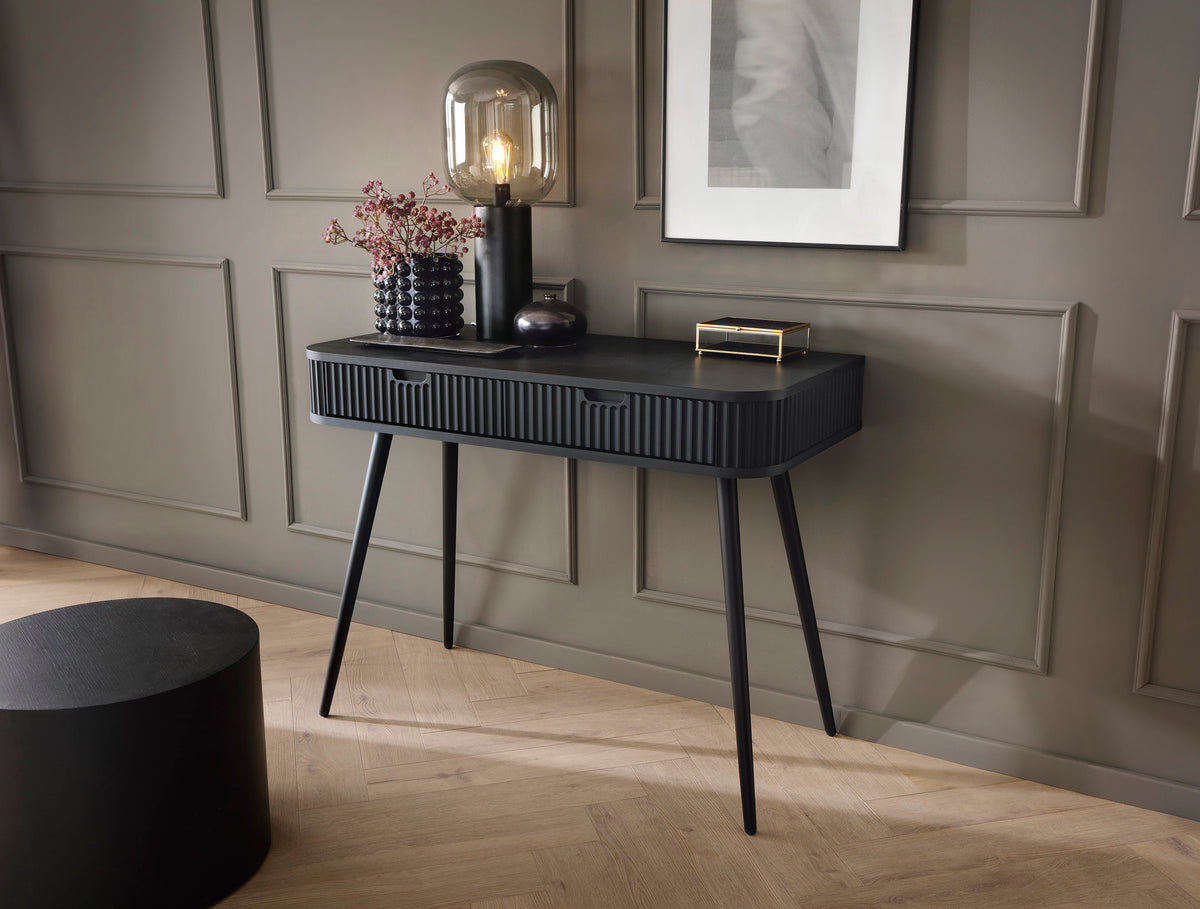 Black dressing table with striped drawer front and black tapered legs in a room setup